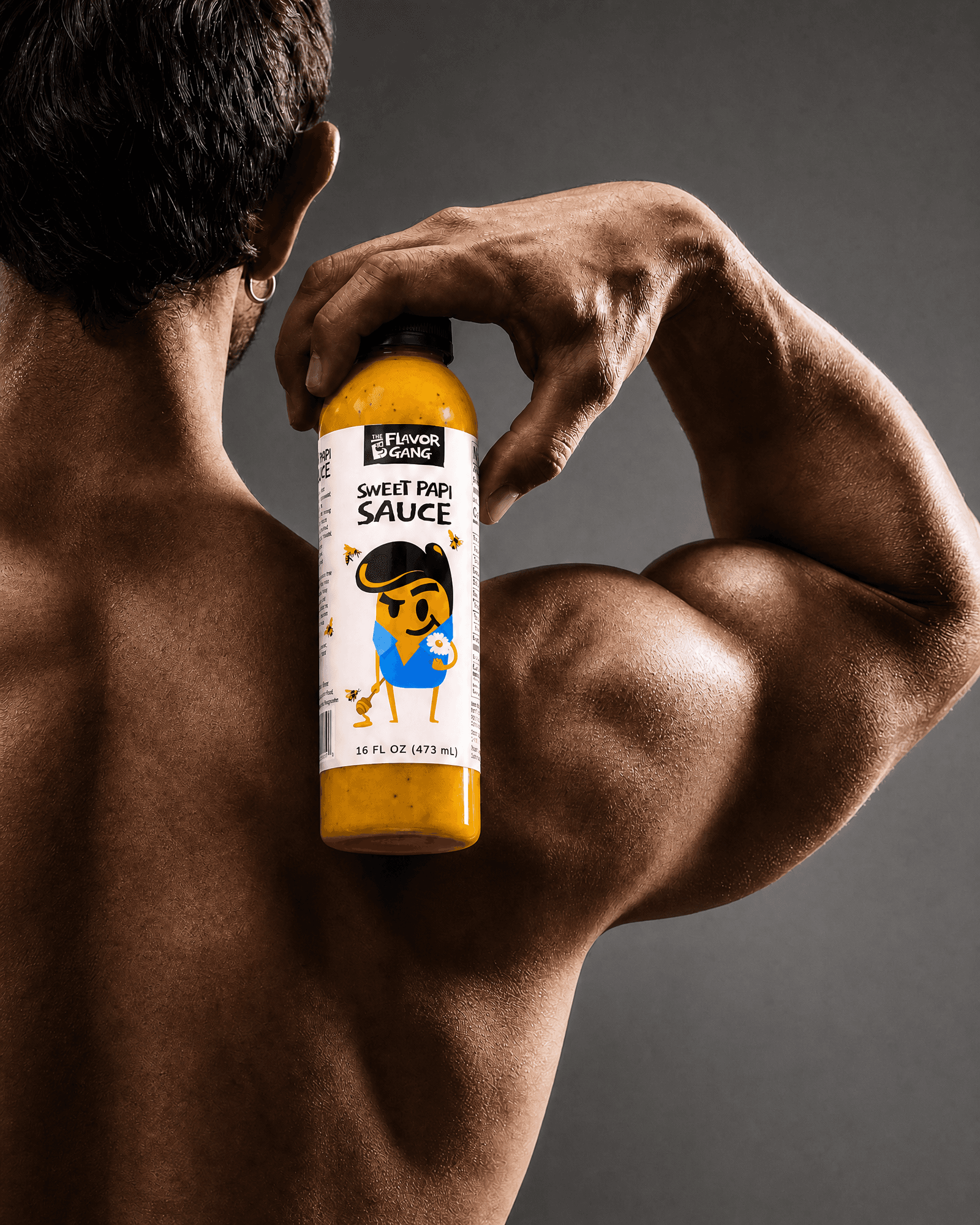 Bodybuilder flexing while holding a bottle of The Flavor Gang Sweet Papi sweet mustard sauce, a macro-friendly workout sauce.