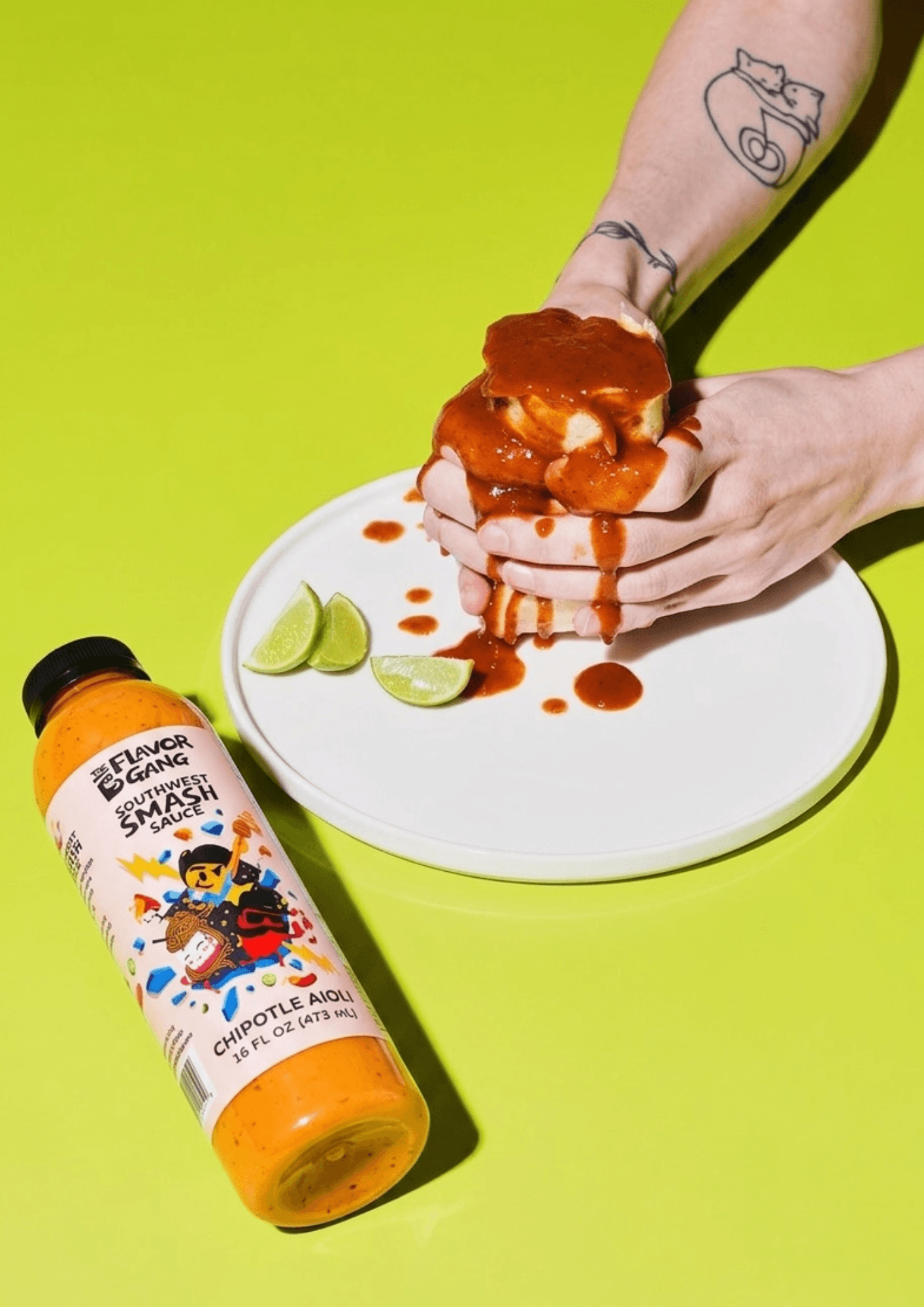 The Flavor Gang Southwest Smash chipotle aioli bottle beside hands smashing a saucy burger on a white plate.